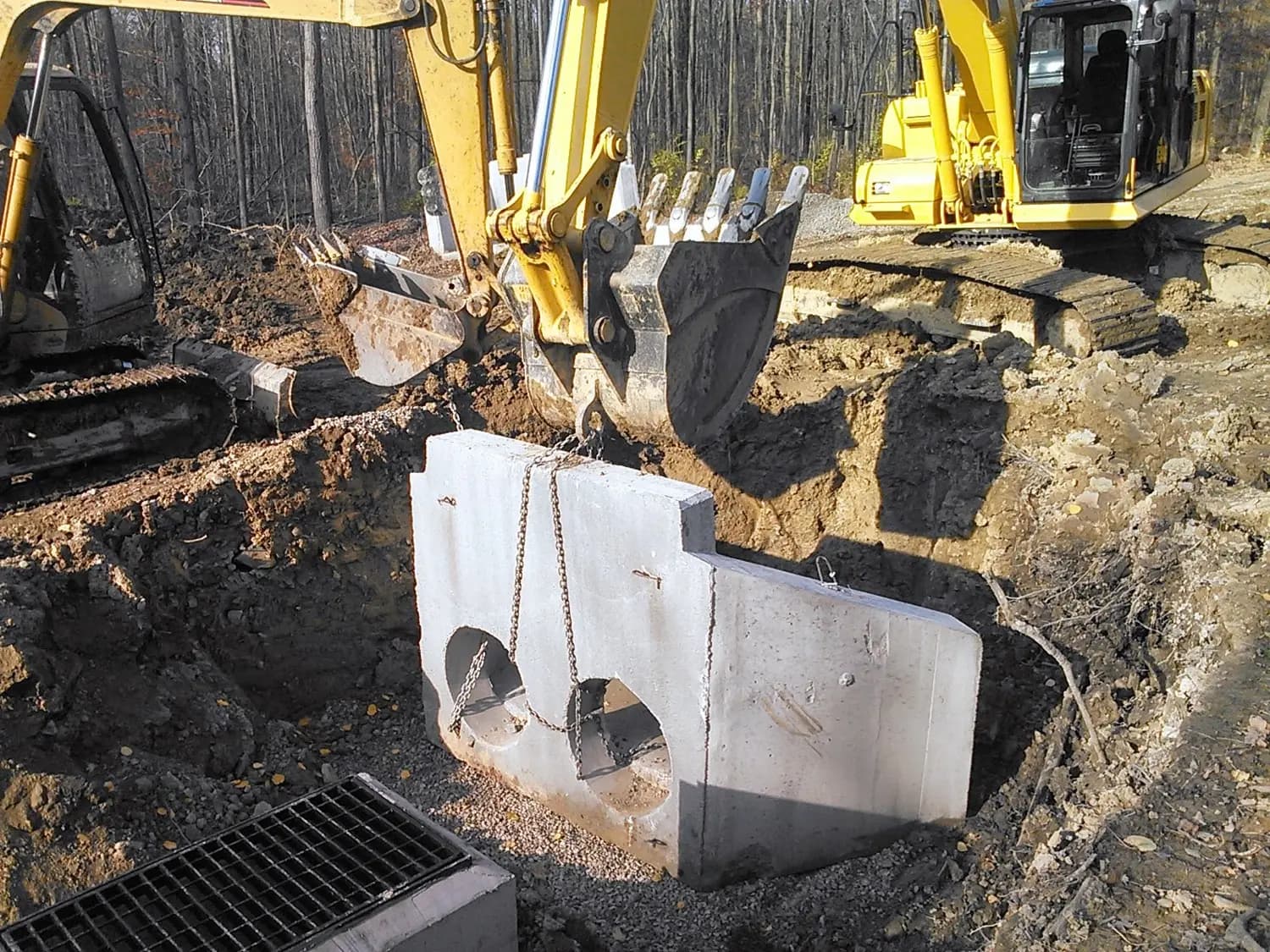 Excavator placing concrete septic tank during installation